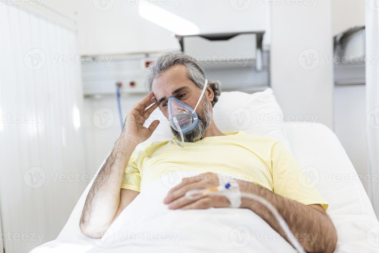 Male coronavirus patient looking away while resting on hospital bed. Man is wearing oxygen mask. He is in hospital during pandemic. photo