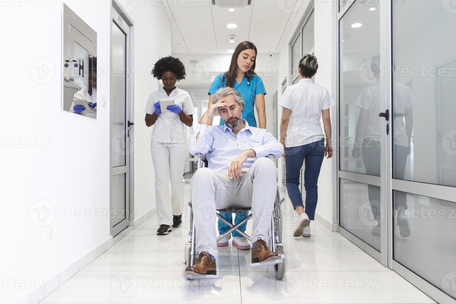 First Floor of the Busy Hospital, Doctors, Nurses and Personnel Busy Working, Assistant Moves Elderly Man in the Wheelchair. New Modern Medical Hospital with Professional Staff. photo