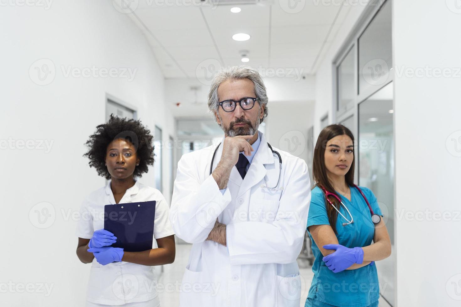 Closeup front view of group of mixed age doctors and nurses standing side by side and looking at the camera. Senior male doctor is standing in front as a leader. photo