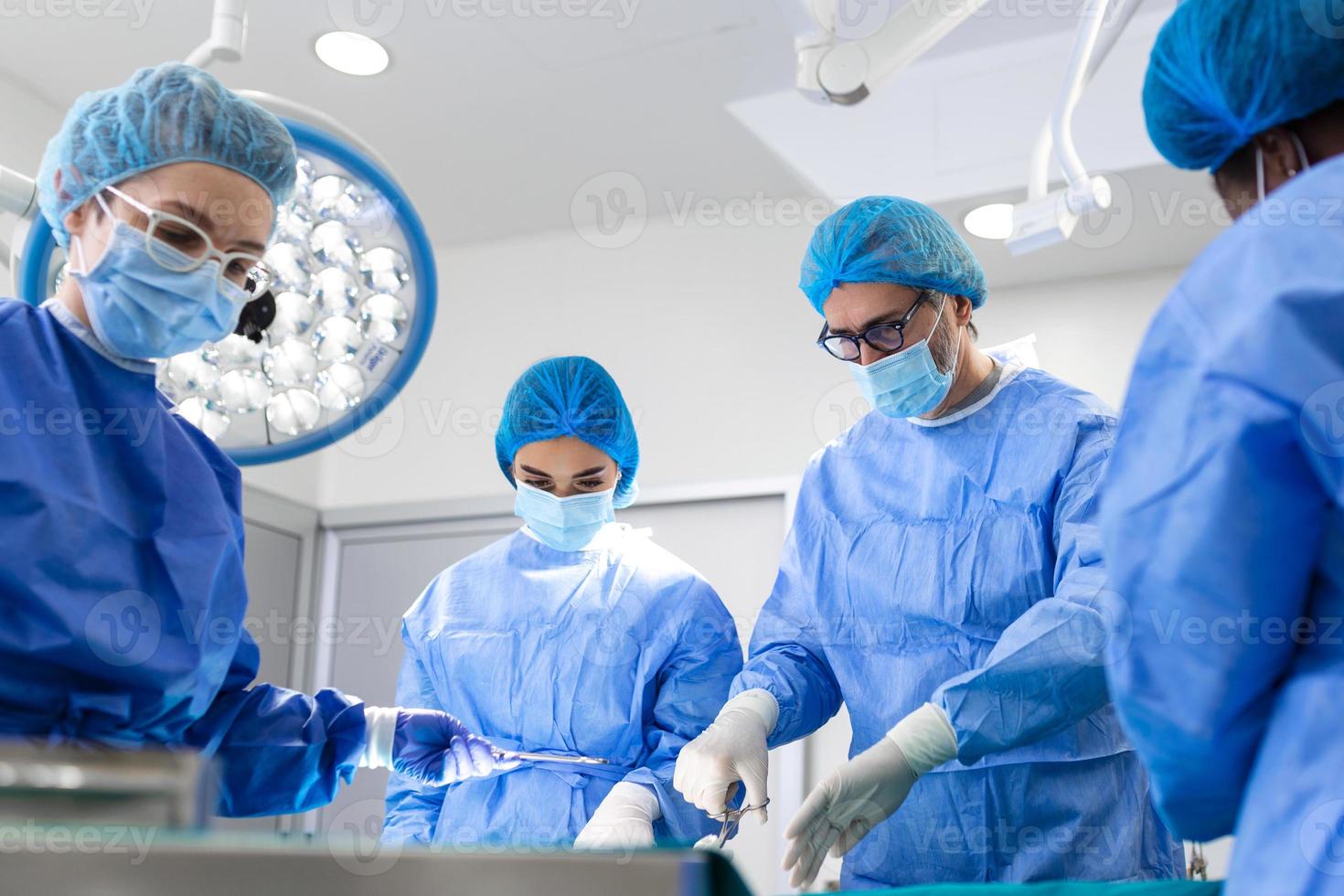 retrato del equipo de cirujanos multiétnicos trabajando en un quirófano. varios médicos que rodean al paciente en la mesa de operaciones durante su trabajo. cirujanos del equipo trabajando en quirófano. foto