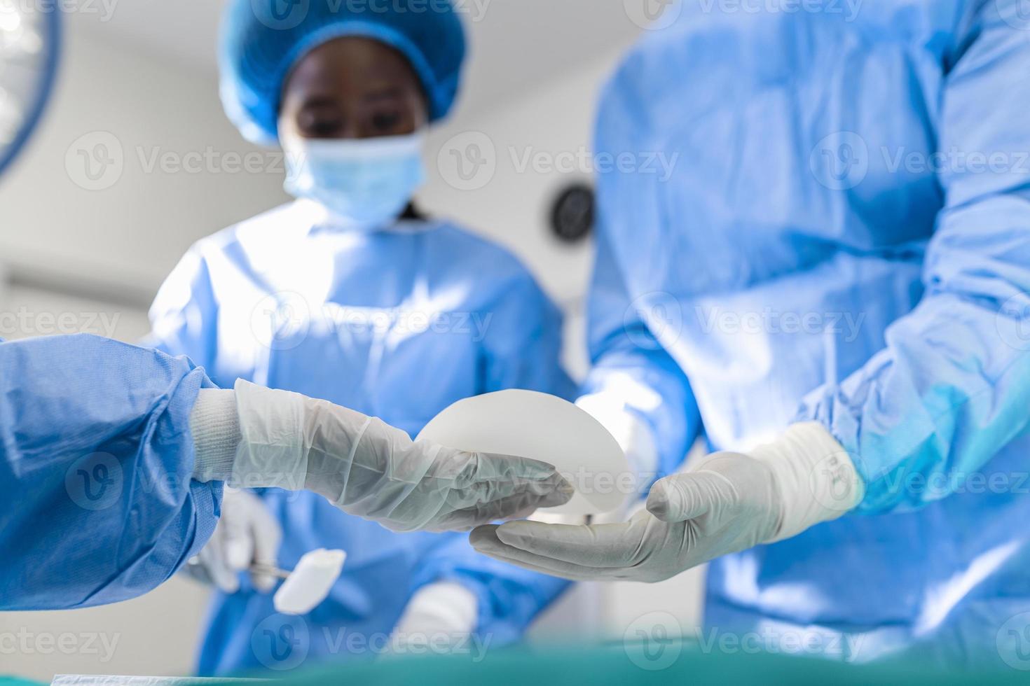 Surgeon and his assistant performing cosmetic surgery in hospital operating room. breast augmentation surgery in the operating room surgeon tools implant. photo