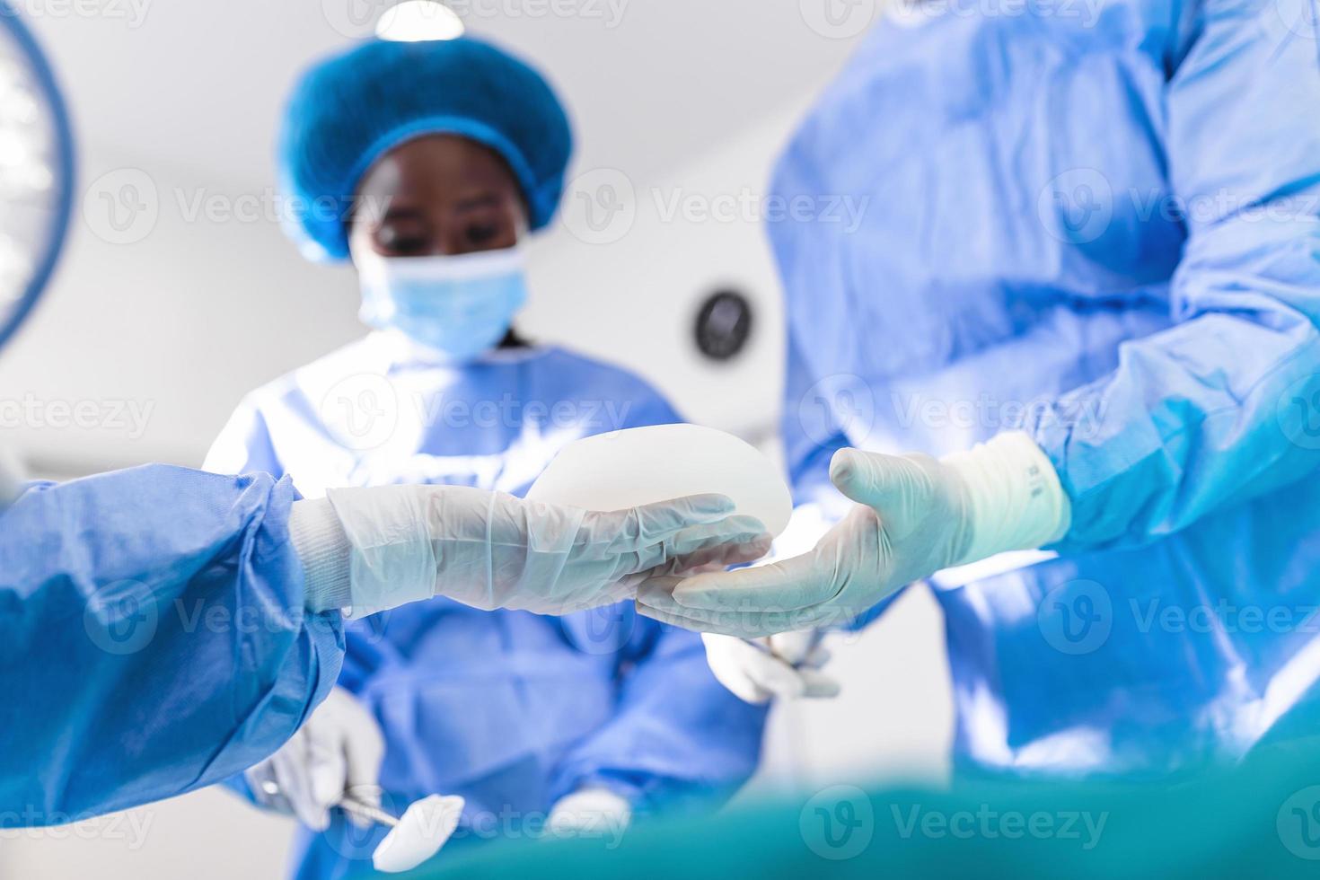 Surgeon and his assistant performing cosmetic surgery in hospital operating room. breast augmentation surgery in the operating room surgeon tools implant. photo