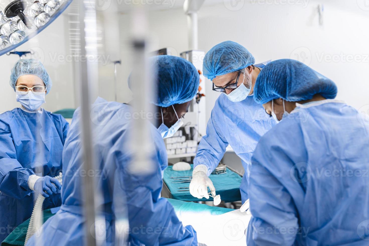 equipo diverso de cirujanos profesionales, asistentes y enfermeras que realizan cirugía invasiva en un paciente en el quirófano del hospital. los cirujanos hablan y usan instrumentos. verdadero hospital moderno. foto