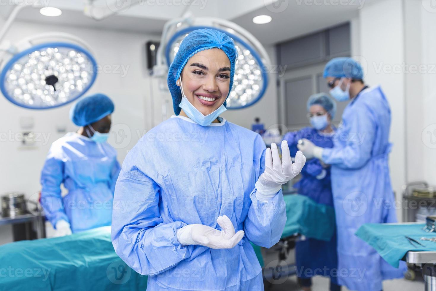 Portrait of female woman nurse surgeon OR staff member dressed in surgical scrubs gown mask and hair net in hospital operating room theater making eye contact smiling pleased happy looking at camera photo