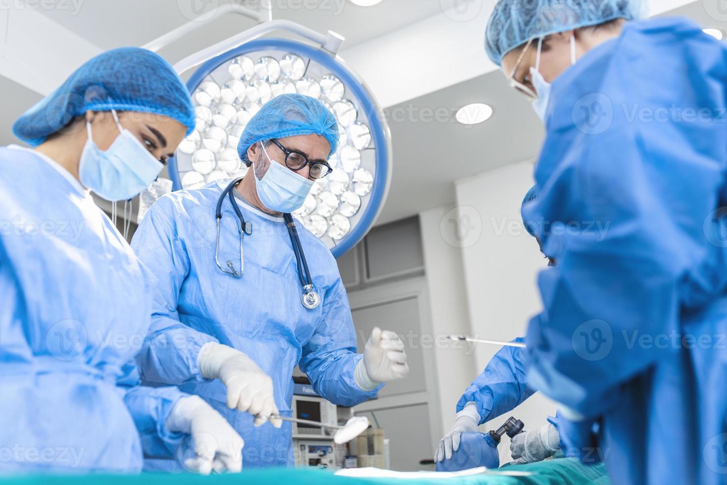 equipo de médicos está de pie en la sala de emergencias. cirujanos multiétnicos están trabajando en el quirófano del hospital. ellos están usando batas azules. foto