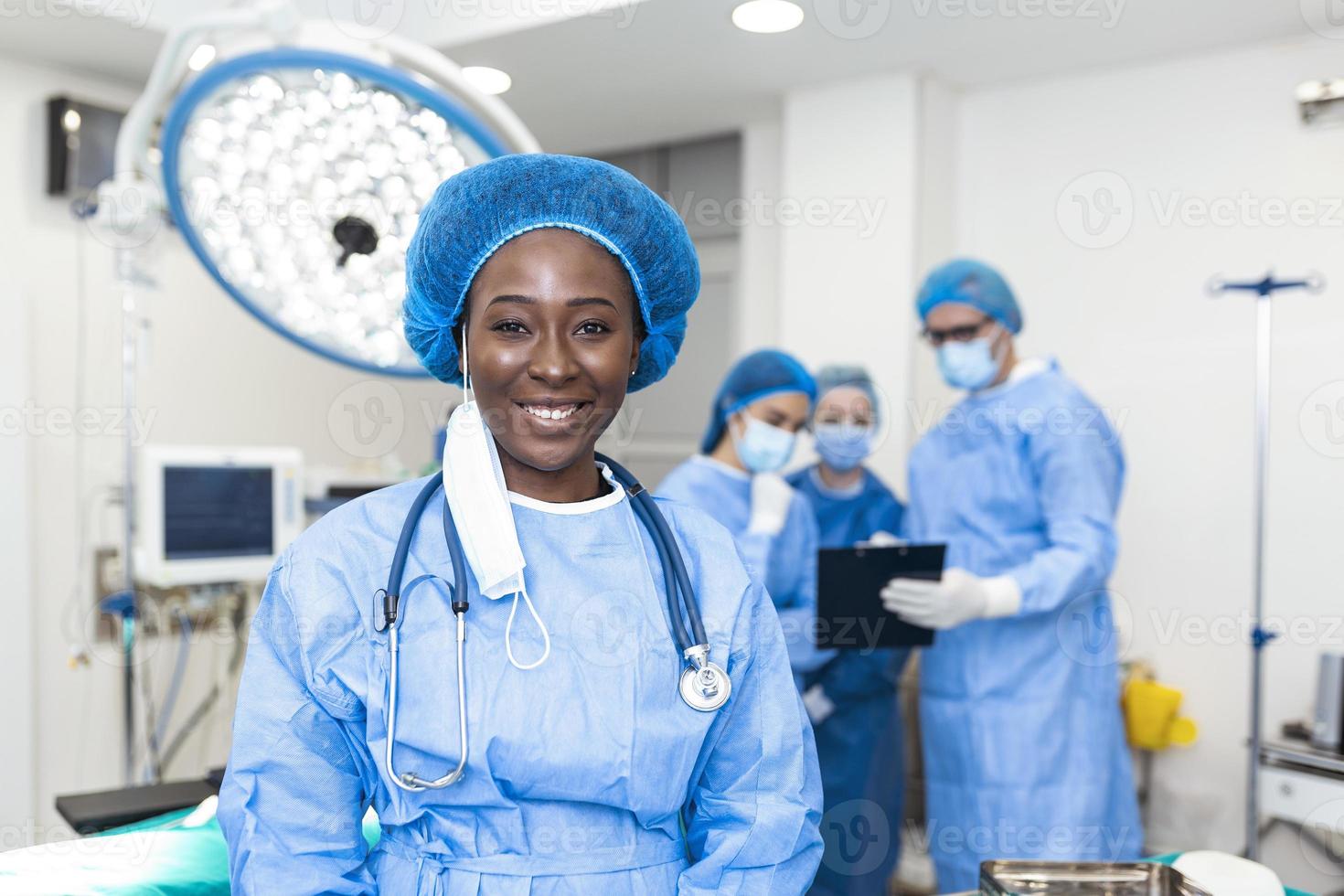 primer plano de una cirujana afroamericana mirando la cámara con colegas actuando en segundo plano en la sala de operaciones. el concepto de medicina foto