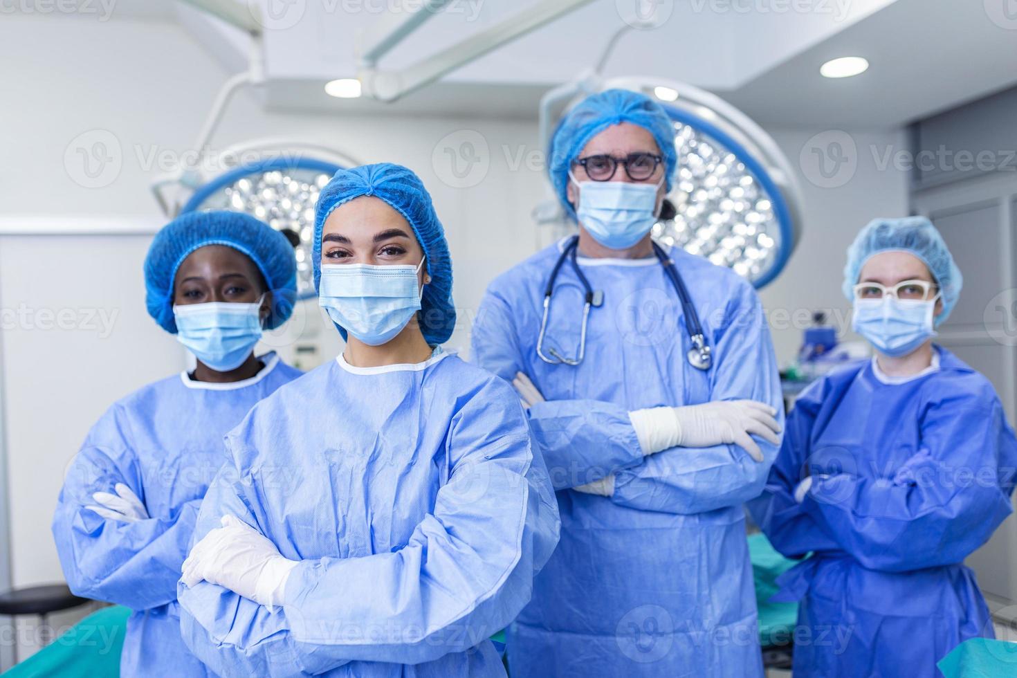 multi-ethnic group of four healthcare workers, a team of doctors, surgeons and nurses, performing surgery on a patient in a hospital operating room. They are looking at the camera. photo