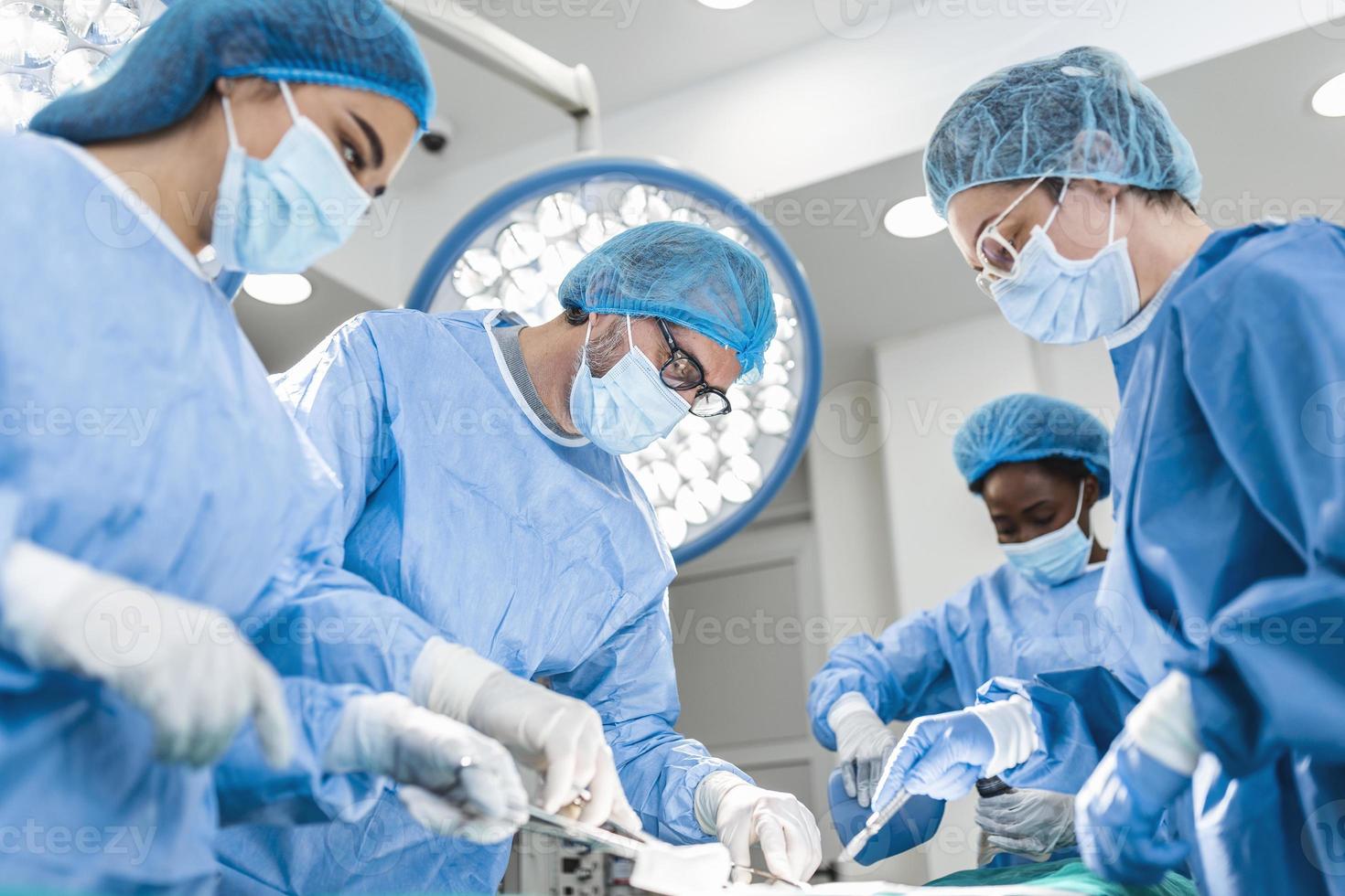 equipo diverso de cirujanos profesionales, asistentes y enfermeras que realizan cirugía invasiva en un paciente en el quirófano del hospital. los cirujanos hablan y usan instrumentos. verdadero hospital moderno. foto