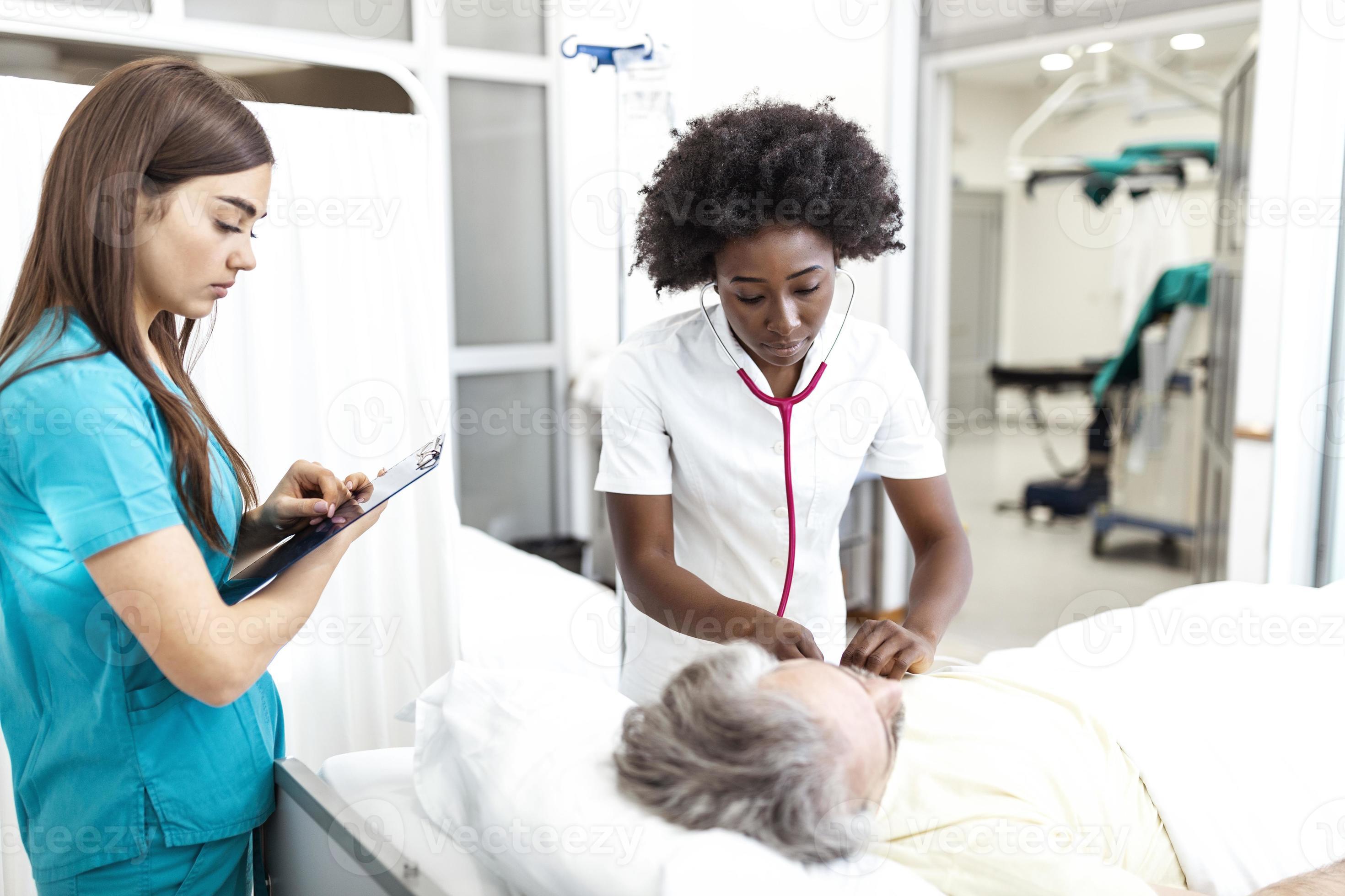 Female doctor and nurse talking to male patient in hospital bed