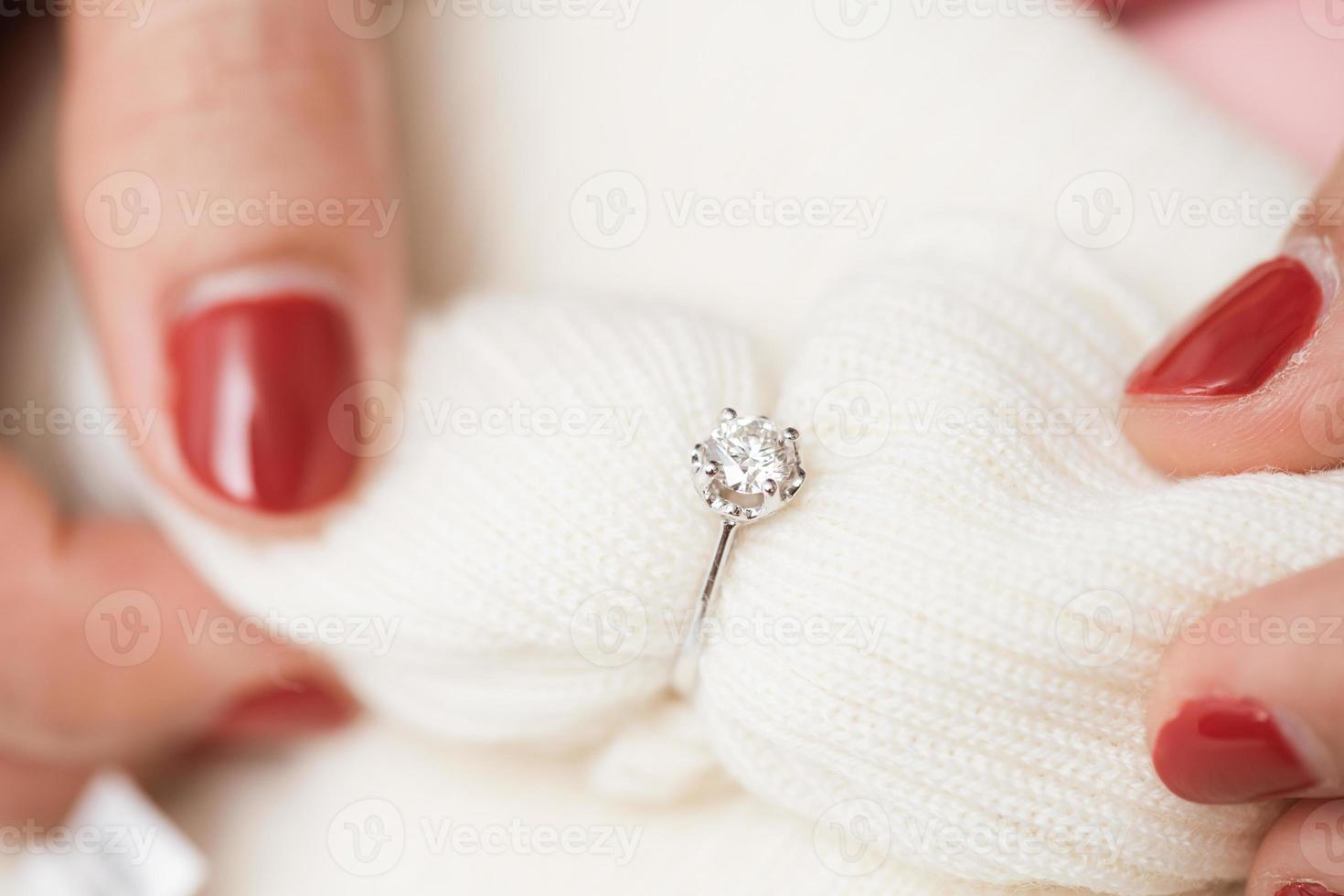 Close up of an elegant engagement diamond ring on woman finger with pink sweater winter clothe. photo