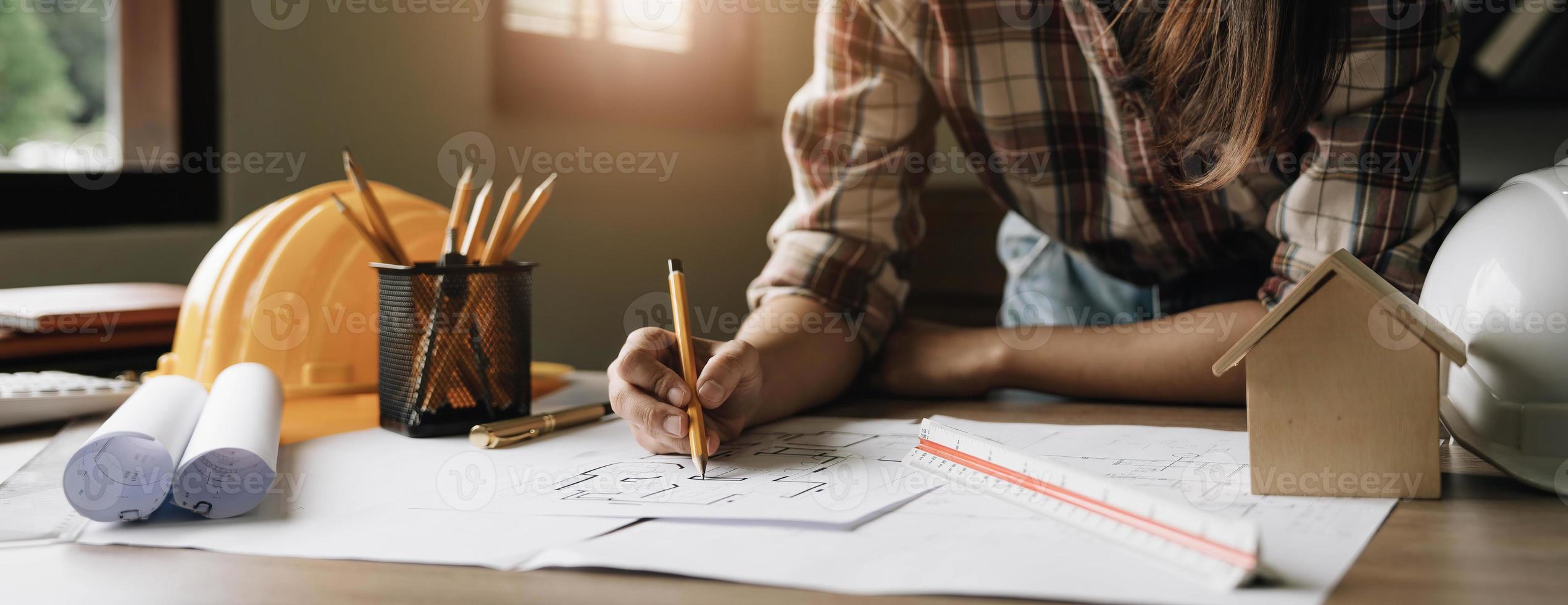 jóvenes ingenieros sosteniendo un bolígrafo rojo apuntando a un edificio en un plano y usando una computadora portátil para escribir una presentación para la reunión en el lugar de trabajo. foto