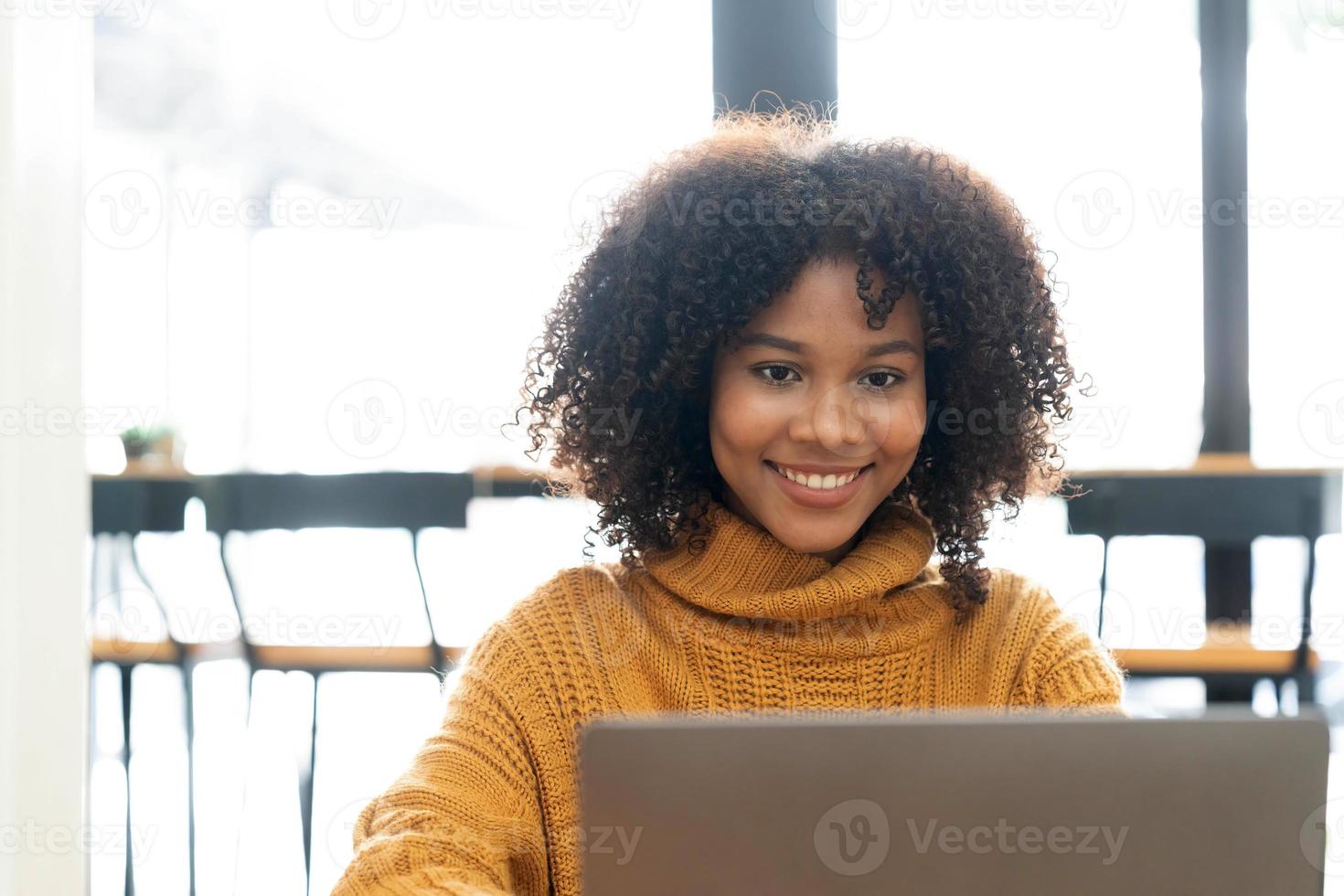 Photo of cheerful joyful mixed-race woman in yellow shirt smiling work on laptop talk speak video  call online. Smart ethnic female in earphones study distant on computer at home. Education concept.