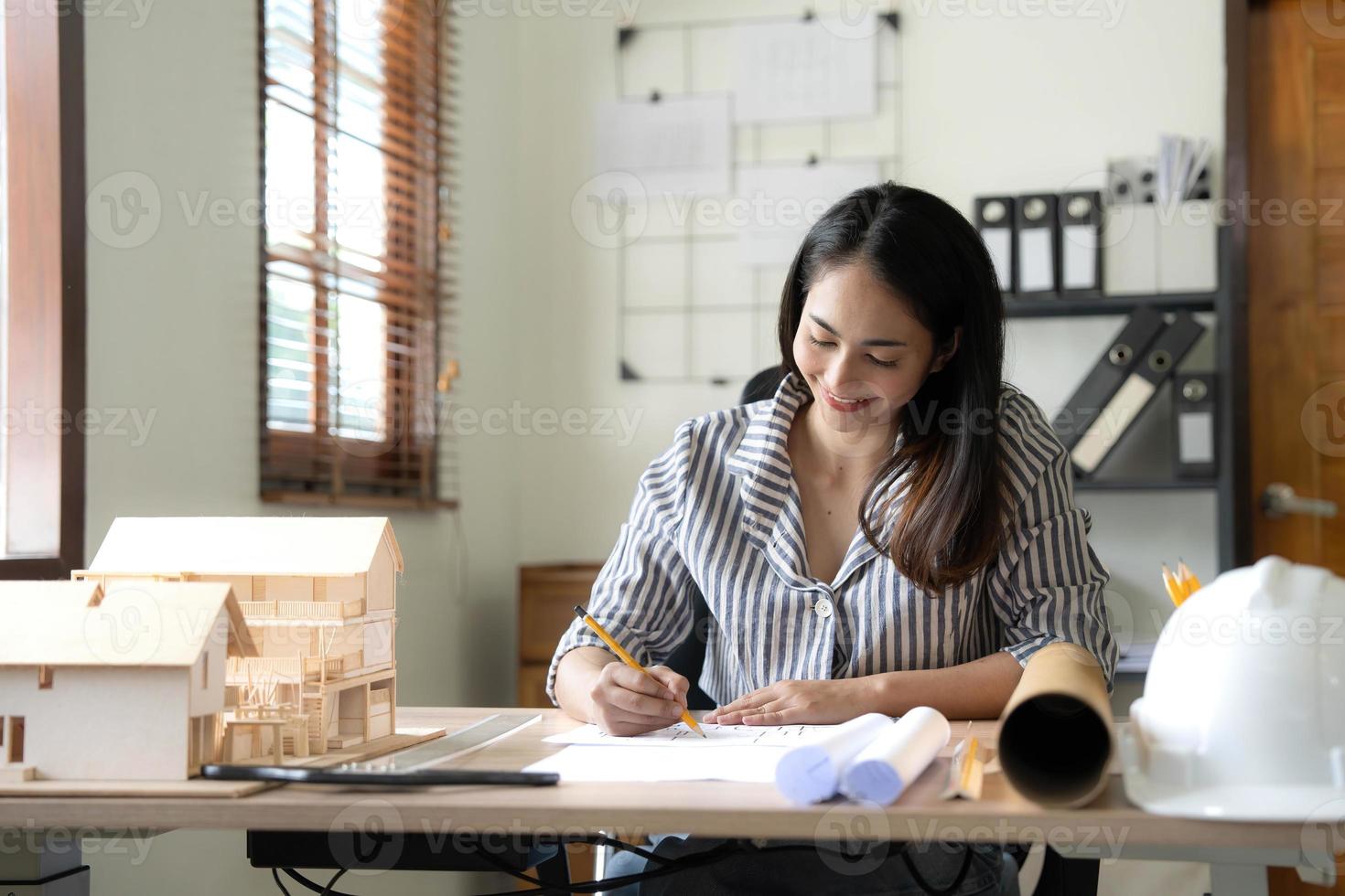 Architecture, building, construction and real estate concept - Happy smiling female architect with blueprint, ruler and living house model on table working at home office. Architect woman. photo