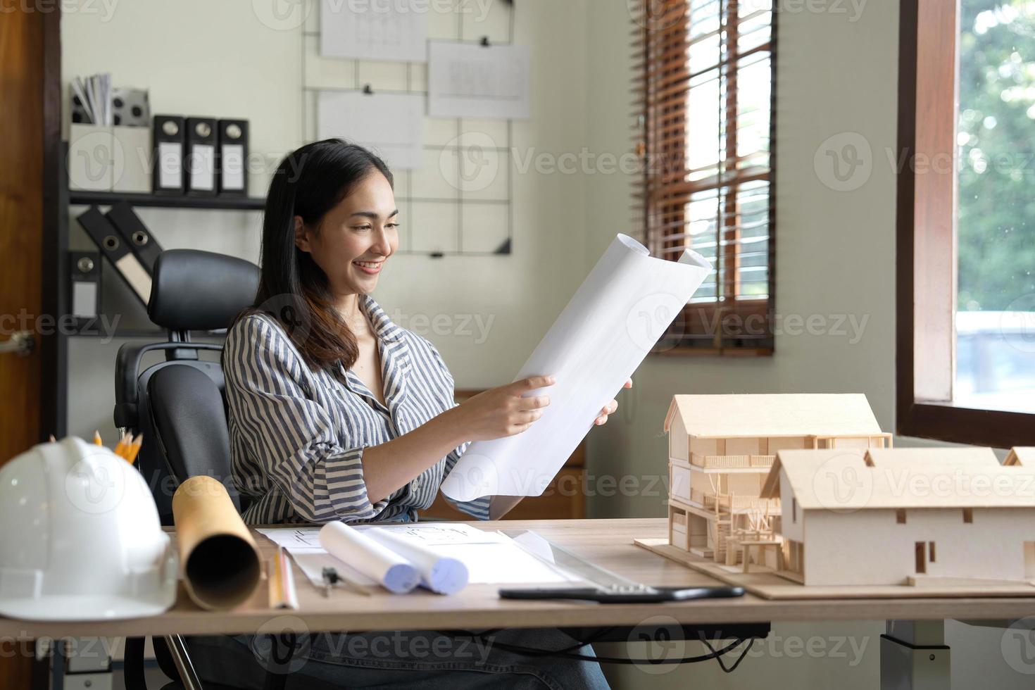 Architecture, building, construction and real estate concept - Happy smiling female architect with blueprint, ruler and living house model on table working at home office. Architect woman. photo