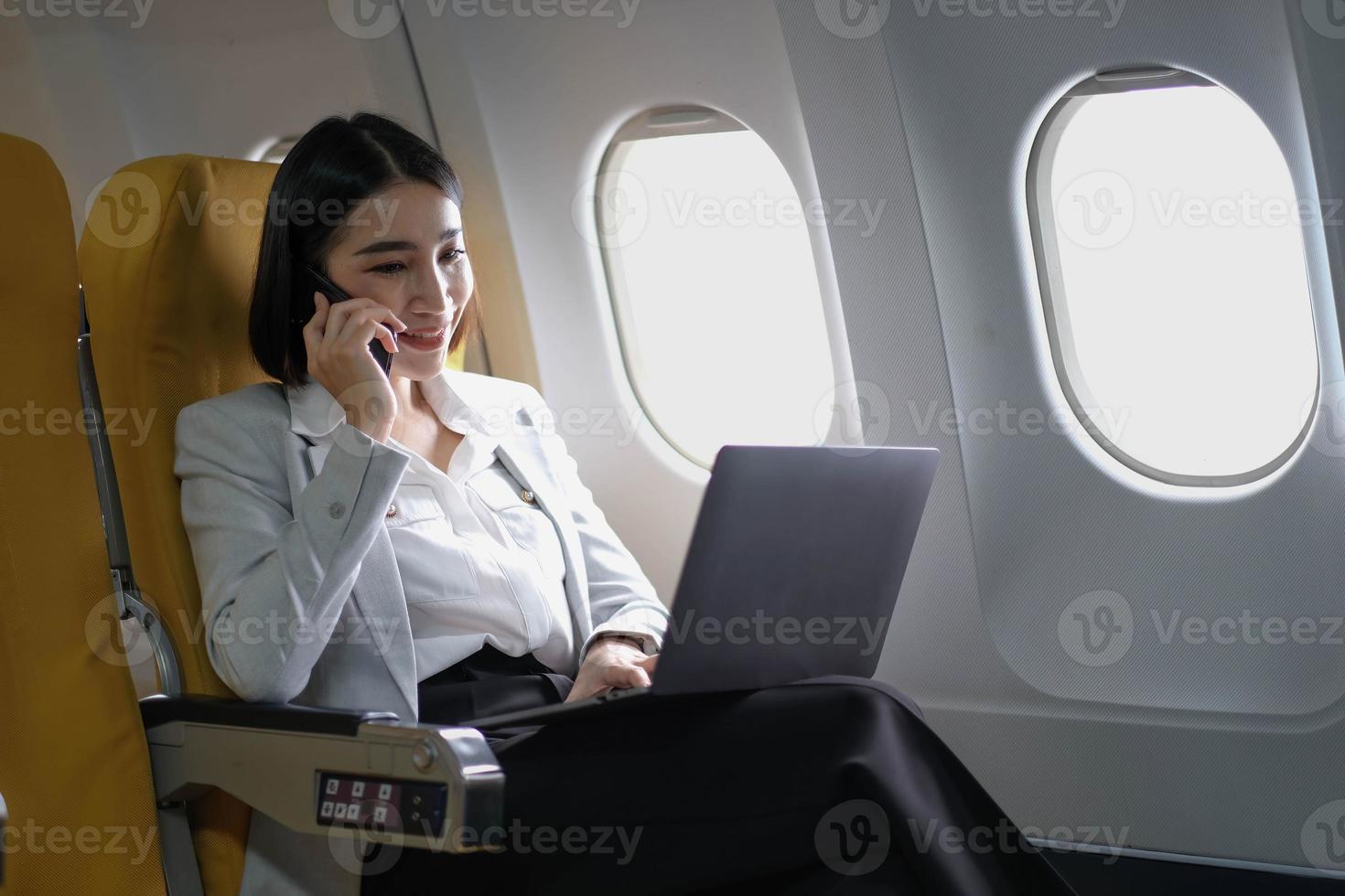 Asian woman passenger sitting in airplane near window and reading news from social networks or using travel applications in smartphone photo