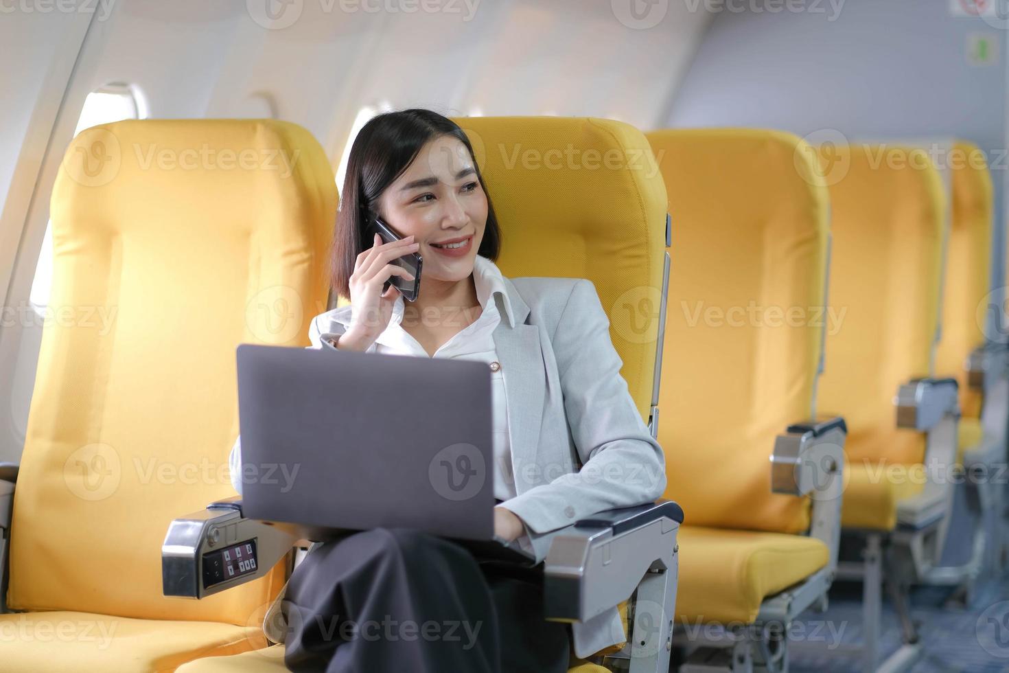 Asian woman passenger sitting in airplane near window and reading news from social networks or using travel applications in smartphone photo