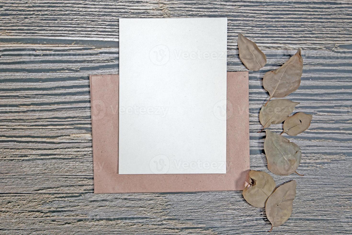A5 paper greeting card mockup with dry leaves on wooden background photo