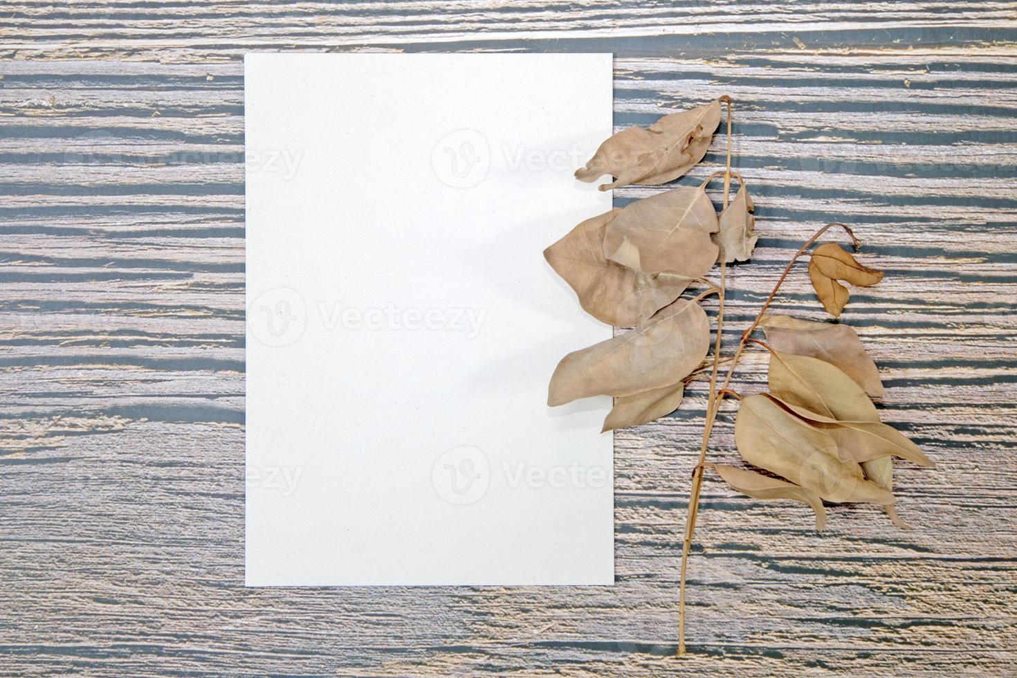 A5 paper greeting card mockup with dry leaves on wooden background photo