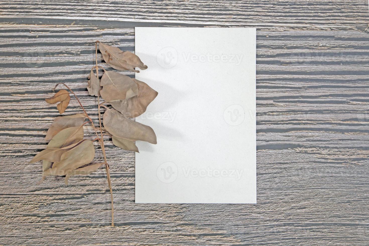 A5 paper greeting card mockup with dry leaves on wooden background photo