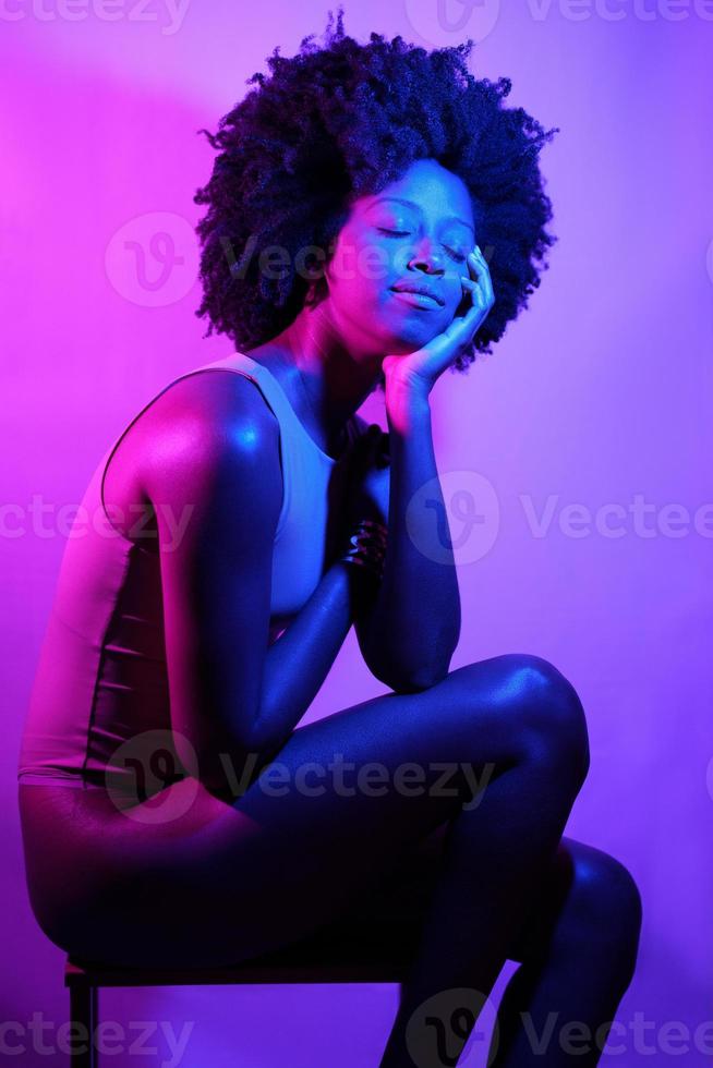 Positive black woman under neon light with eyes closed. photo