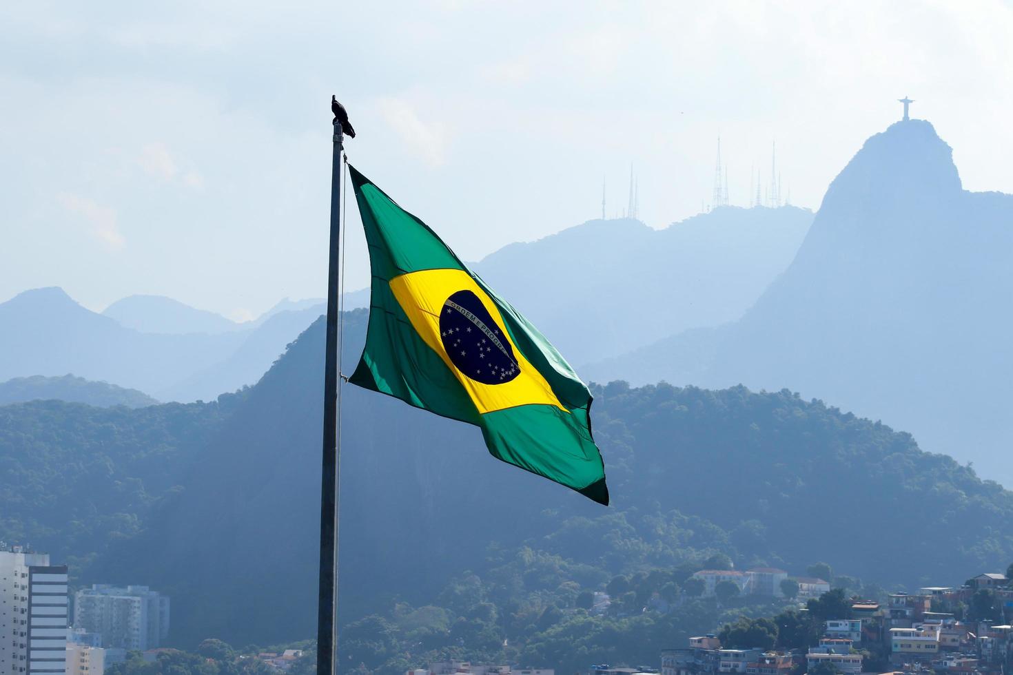 Rio de Janeiro, RJ, Brazil - April 27, 2022 - Brazilian flag waves with Corcovado hill and Christ the Redeemer Statue at background - Duque de Caxias Fort, Leme neighborhood photo
