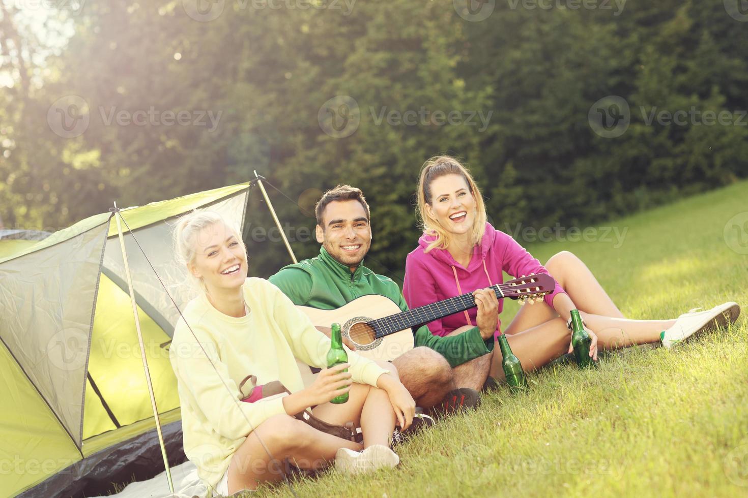 Group of friends camping in forest and playing guitar photo