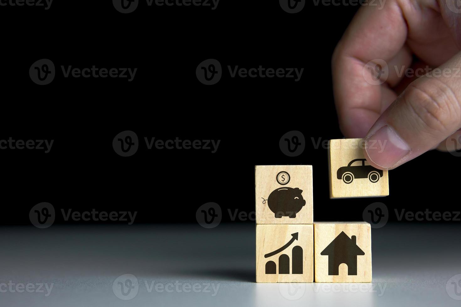 Concept of financial planning and investing for the future. Hand picking wooden blocks with icons, piggy bank, graph, house and car. with copy space for text or design for business photo
