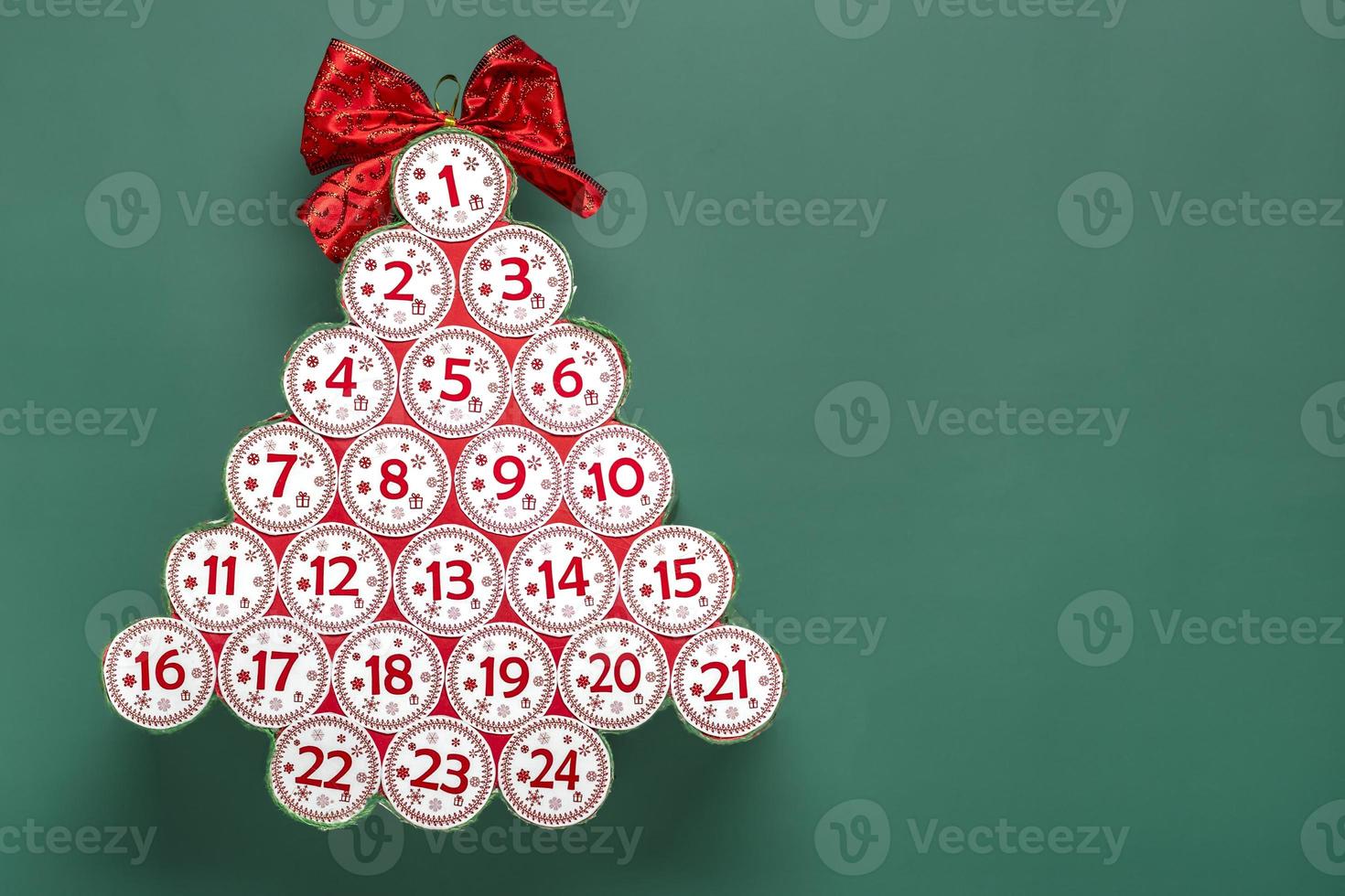 Advent calendar in shape of Christmas tree with numbers and ribbon instead of star, bokeh light on green background Xmas advent calendar concept Top view Holiday card photo