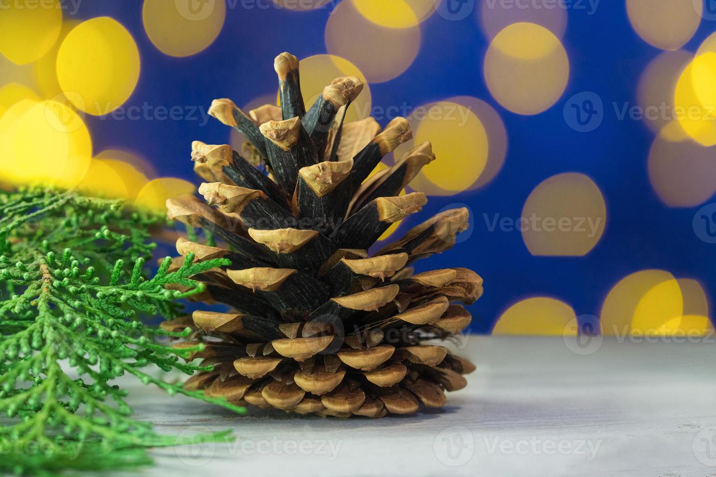 Big cone on the table with thuja branch. Yellow bokeh on blue background. Merry Christmas and New year card photo