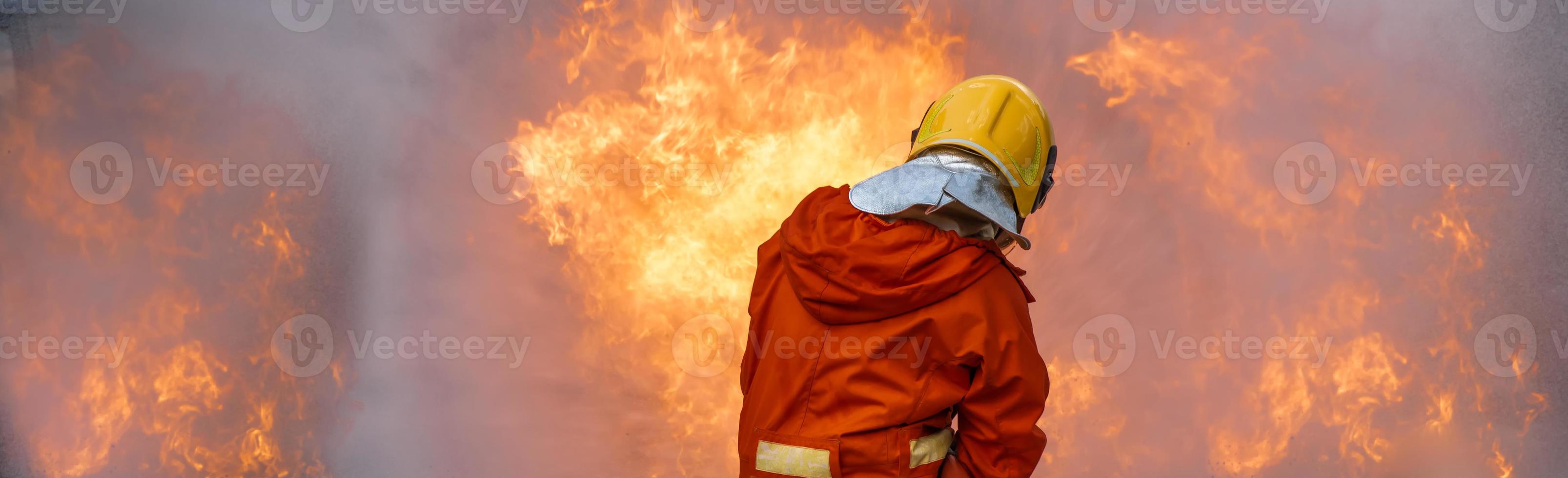 Firefighter Rescue training to stop burning flame, Fireman wear hard hat and safety uniform suit for protection burn using hose with chemical water foam spray. photo