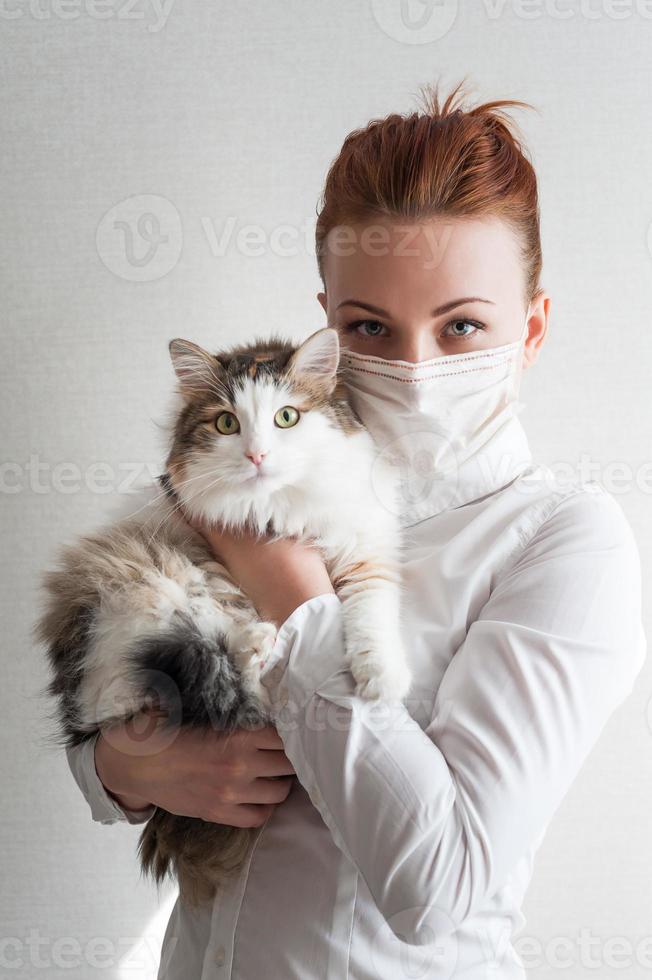 Portrait of a girl in a medical mask. She is holding a pet cat. Close up photo