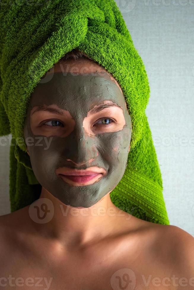 Young woman with clay mask on her face against light background, space for text. photo