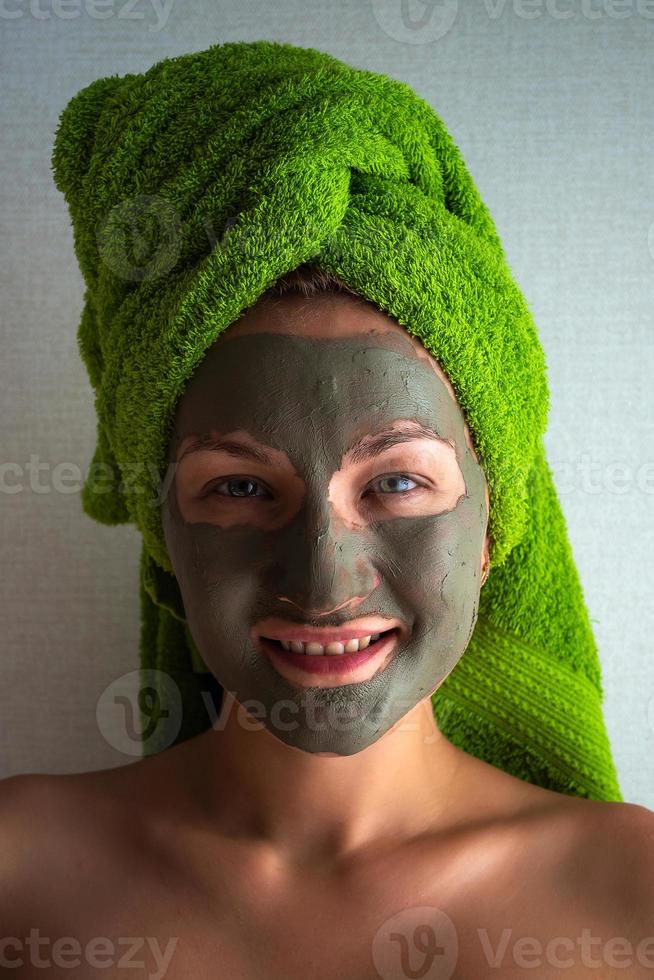 Young woman with clay mask on her face against light background, space for text. photo