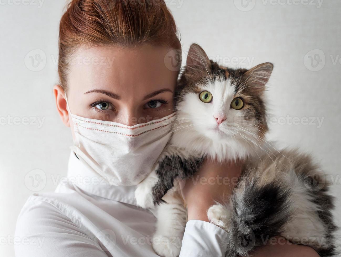 Portrait of a girl in a medical mask. She is holding a pet cat. Close up photo