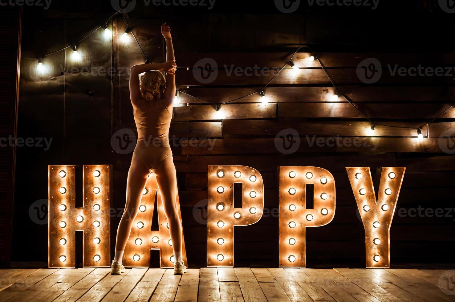 A girl in a swimsuit and sneakers is sitting on the floor. The word happiness is highlighted in large bright letters photo