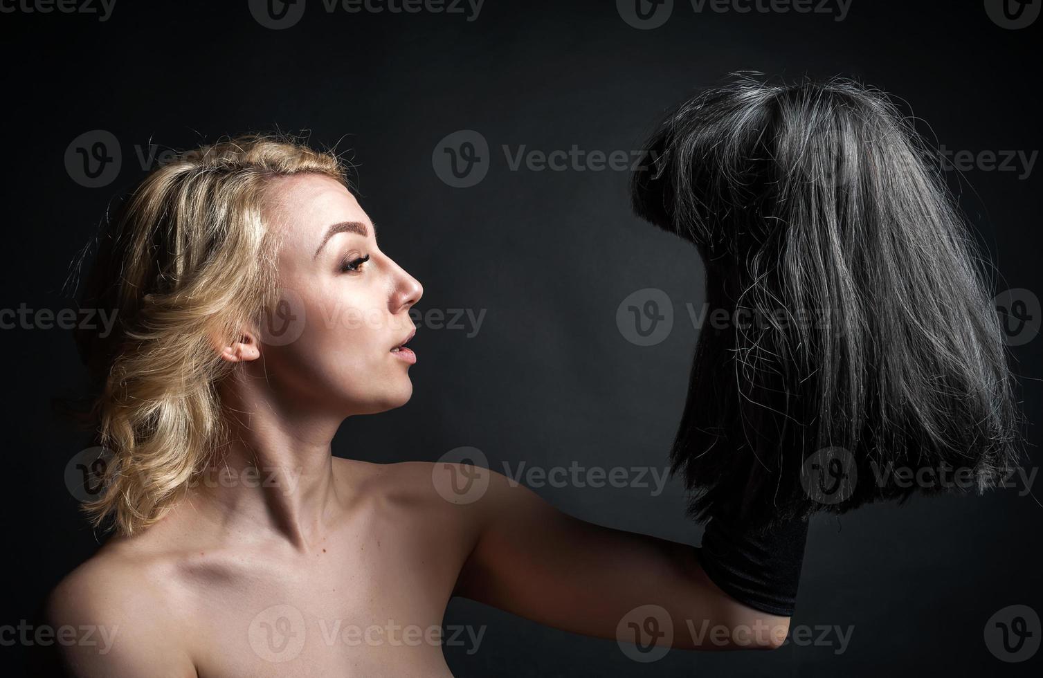 a young blonde woman with a wig, holding a black wig in her hand. on black background photo