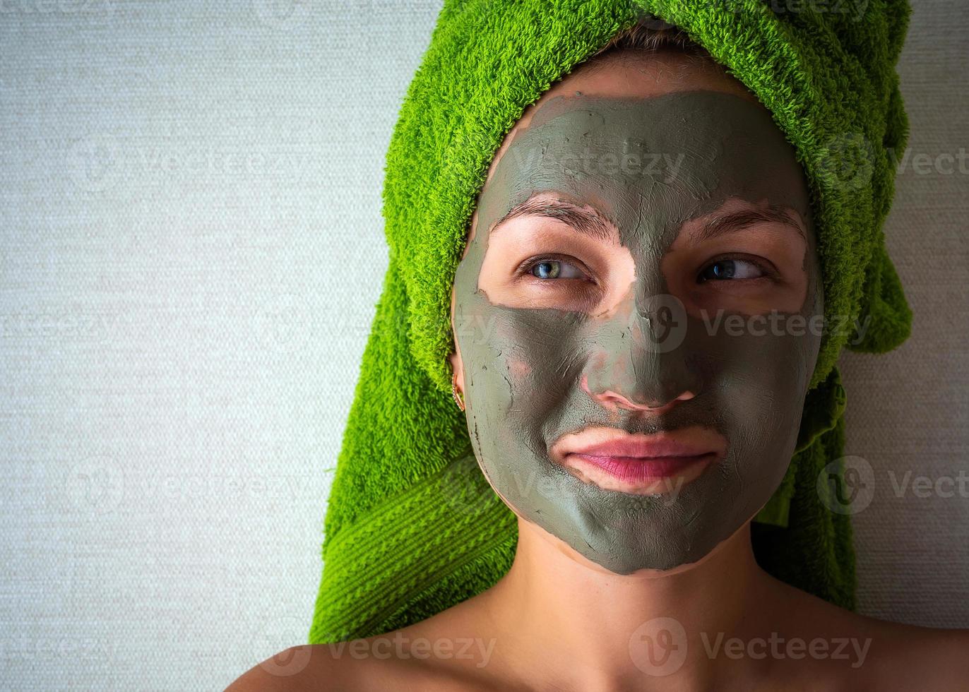 Young woman with clay mask on her face against light background, space for text. photo