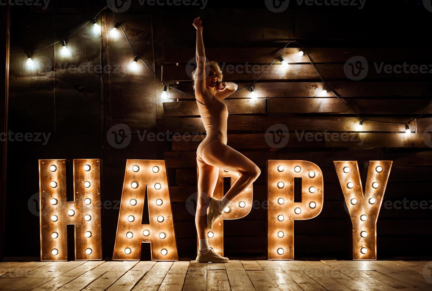 A girl in a swimsuit and sneakers is sitting on the floor. The word happiness is highlighted in large bright letters photo