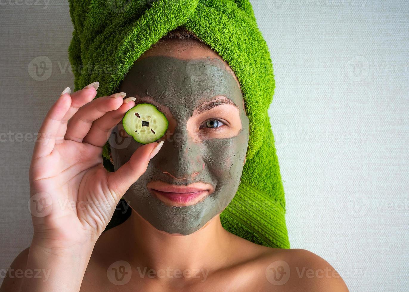 Beautiful young woman with facial mask on her face holding slices of cucumber. photo