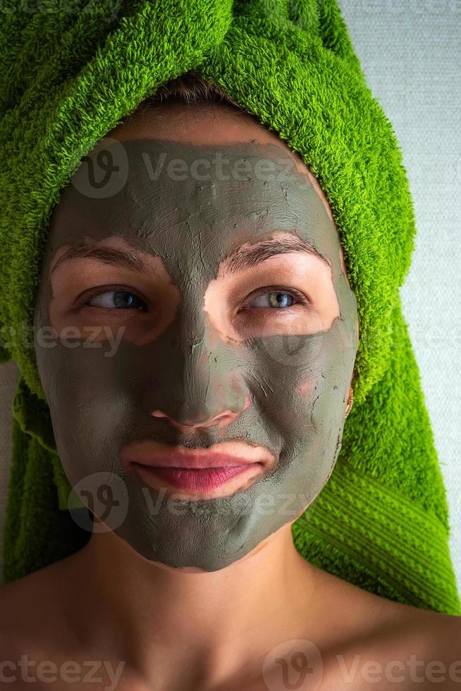 Young woman with clay mask on her face against light background, space for text. photo