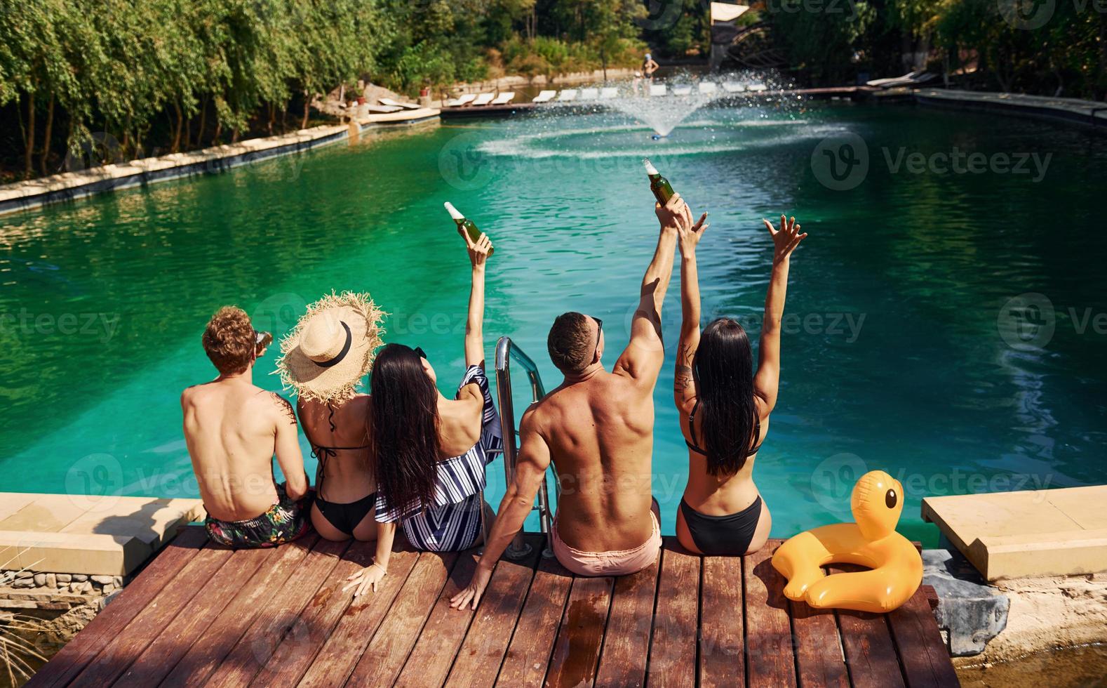 descansando juntos. un grupo de jóvenes felices se divierten en la piscina durante el día foto