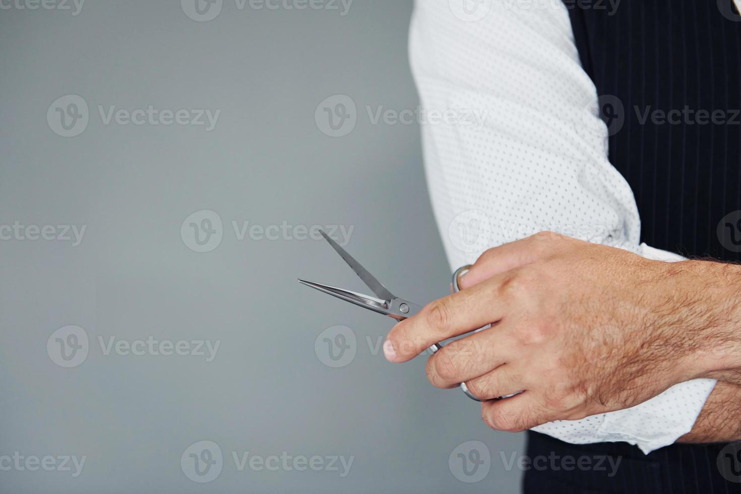 Close up view of man in luxury clothes that standing indoors in barbershop with scissors photo