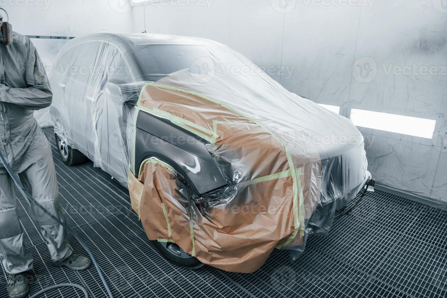 Covering car by brown cloth. Caucasian automobile repairman in uniform works in garage photo