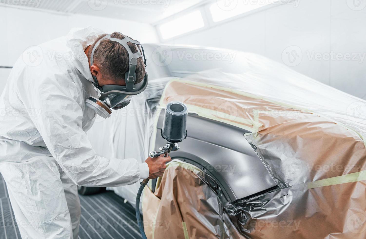 Painting job in progress. Caucasian automobile repairman in uniform works in garage photo
