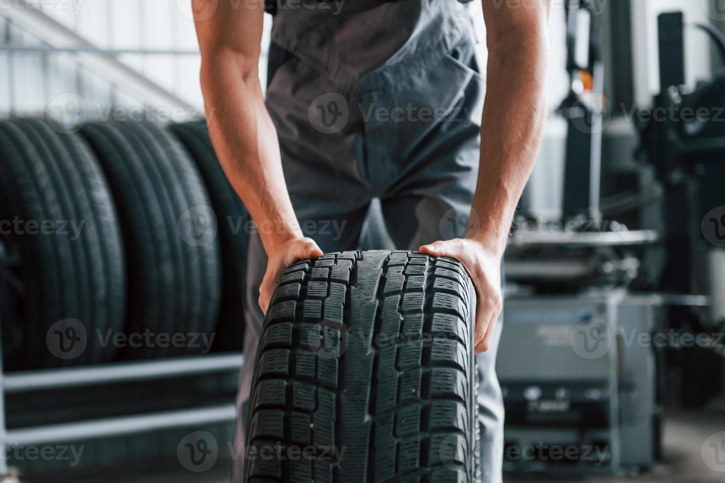 rueda el neumático. hombre adulto con uniforme de color gris trabaja en el salón del automóvil foto