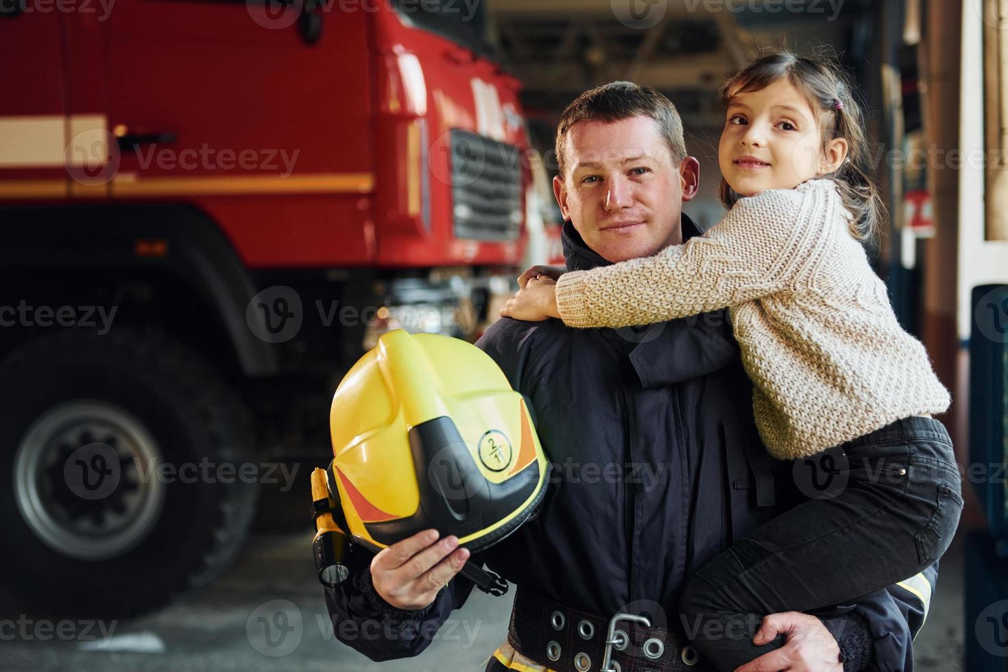 Happy little girl is with male firefighter in protective uniform photo