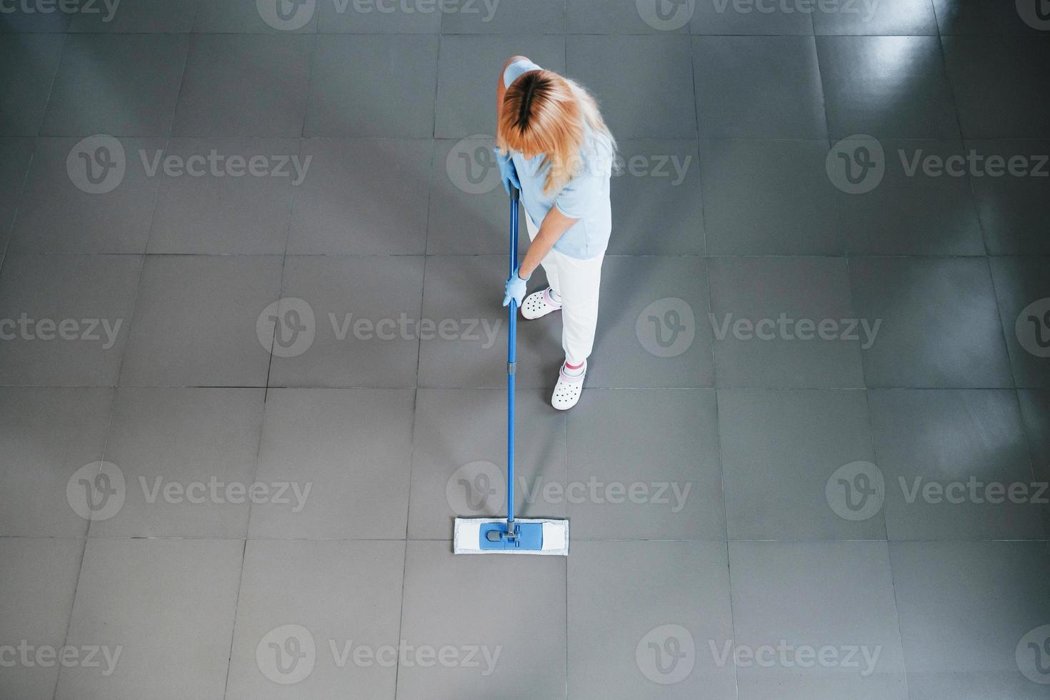 Top view of woman in blue shirt and protective gloves that uses vacuum cleaner photo