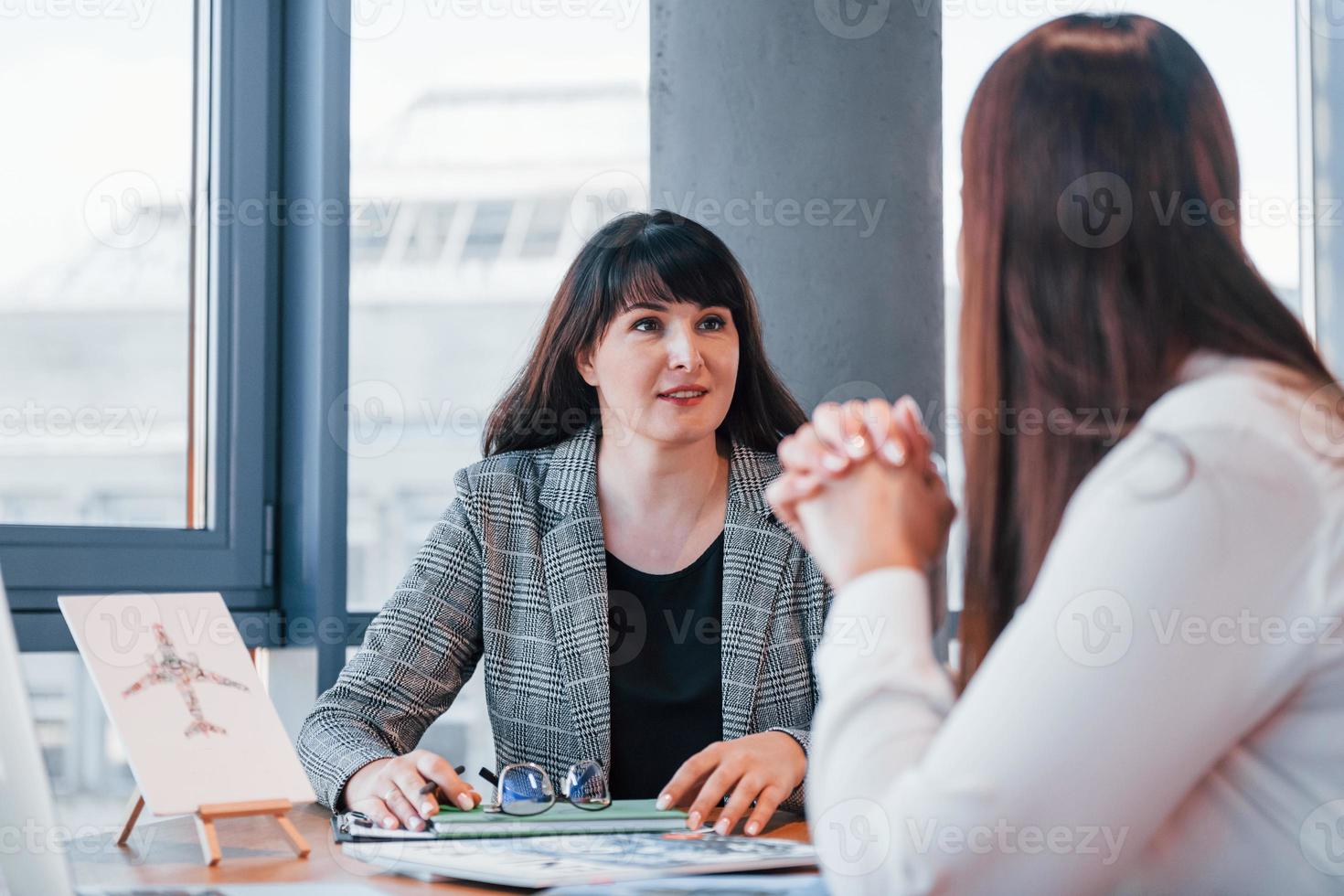 sentado junto a la mesa. dos mujeres con ropa formal están adentro en la oficina moderna trabajando juntas foto