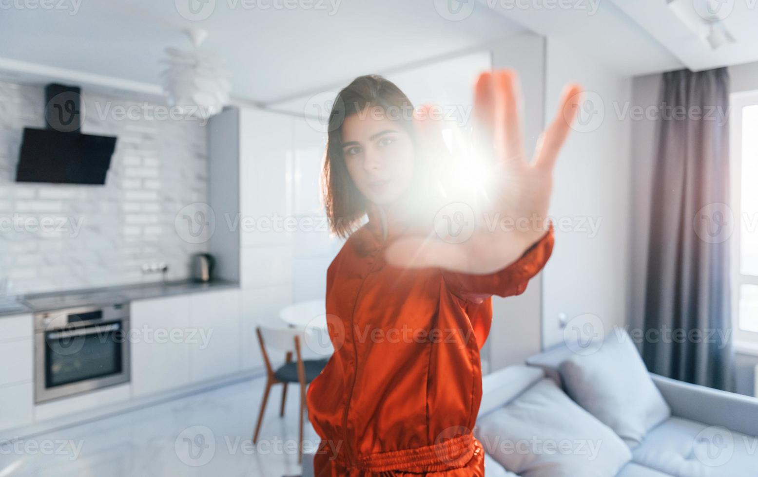 Posing for a camera in red costume. Young woman is indoors in room of modern house at daytime photo