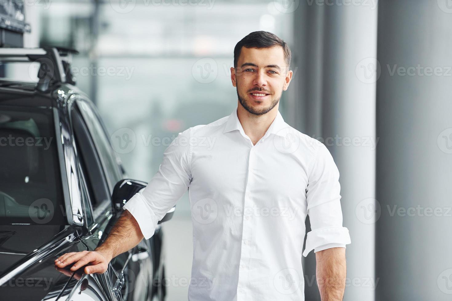 un joven con camisa blanca está adentro con un automóvil nuevo y moderno foto